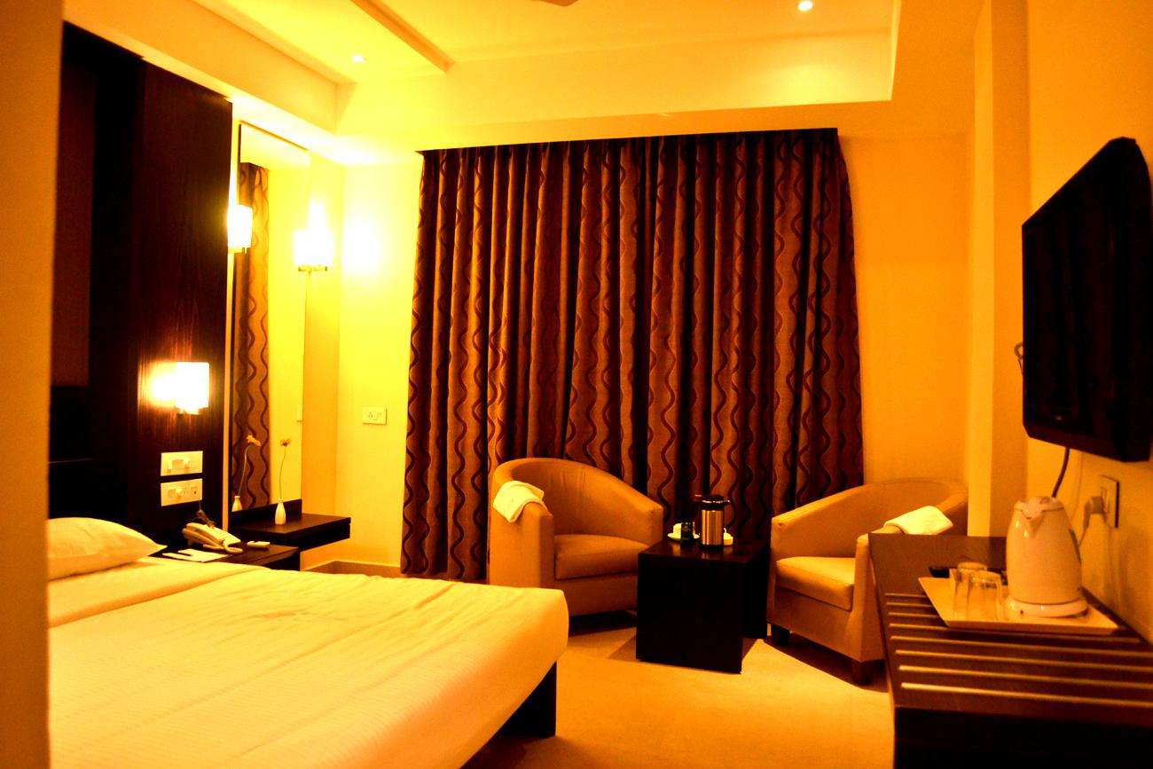 Hotel room interior at Tiruppur, Tamilnadu, featuring a cozy setup with warm ambient lighting, modern furniture, full-length curtains— done by hotel interior designers, furniture suppliers, and turnkey hospitality contractors.