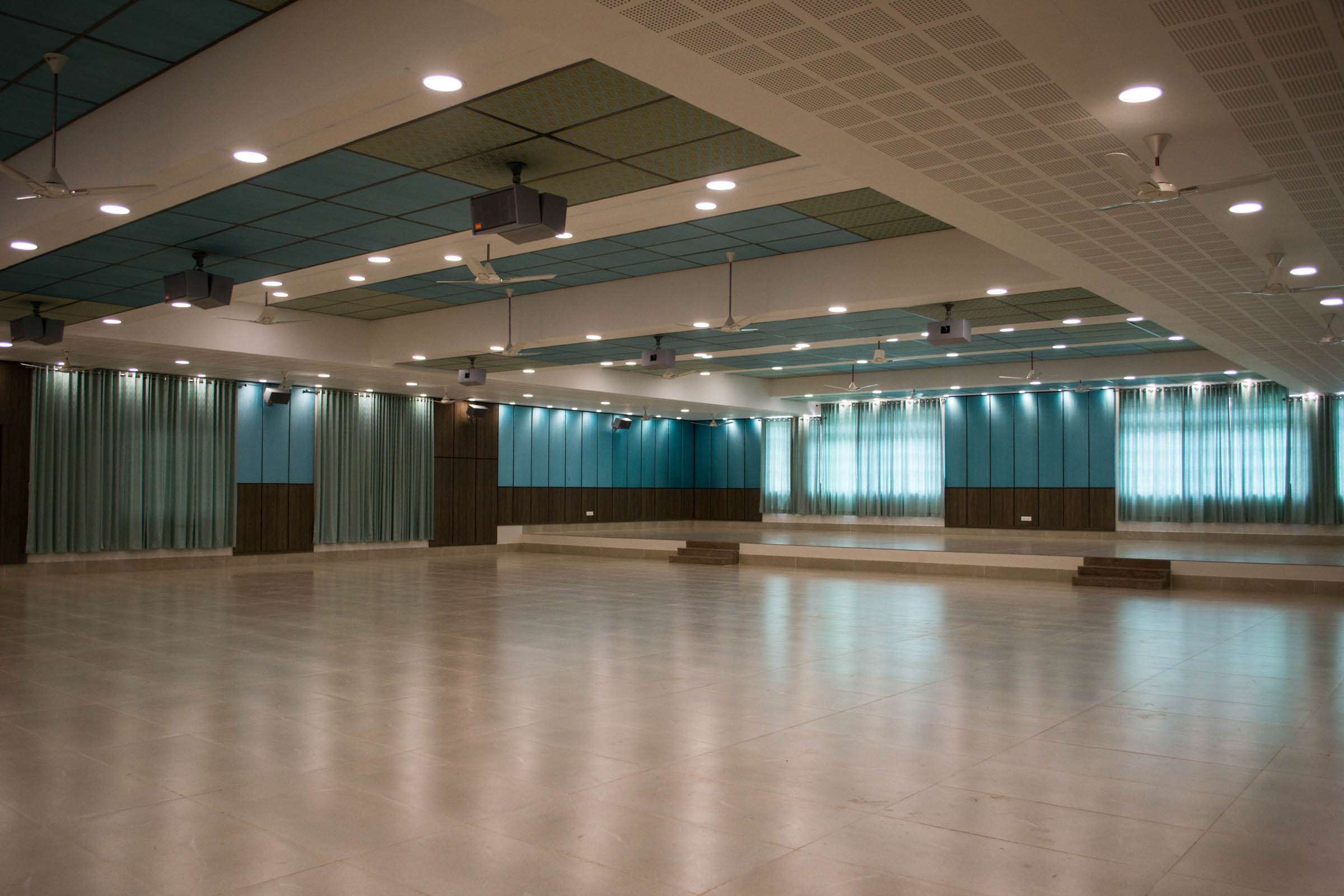 Spacious and modern meeting hall in a convention centre featuring acoustic ceiling panels, ambient lighting, and teal curtains – conferences and large gathering space designers, acoustic panel manufacturers and installers— this project is at Yercaud, Salem.