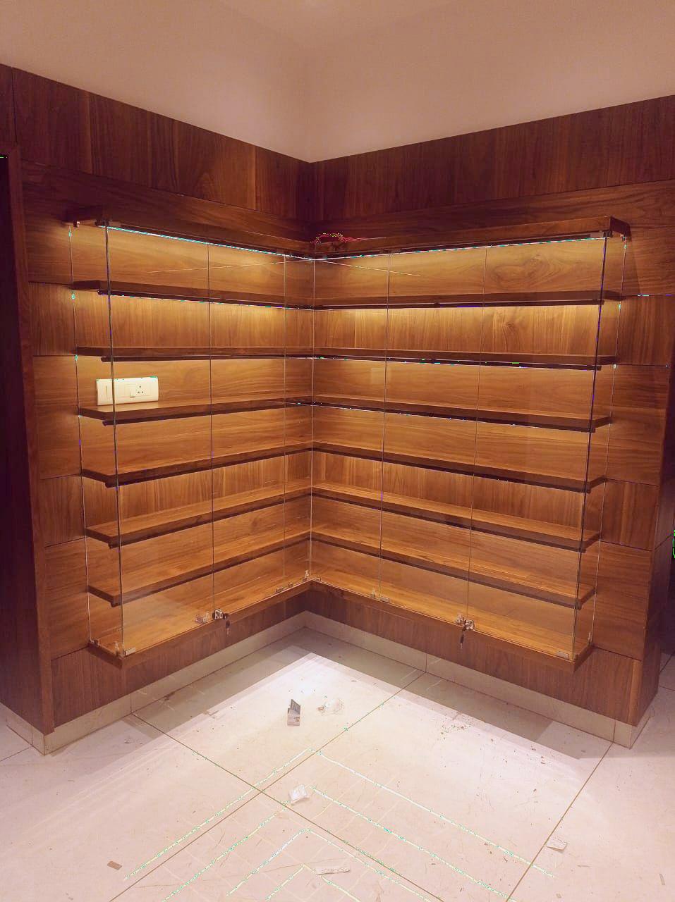 Custom-built wooden corner display unit with glass shutters and LED strip lighting, designed for showcasing collectibles at a residence in Avinashi Road, Coimbatore – crafted by expert interior designers and furniture installers.