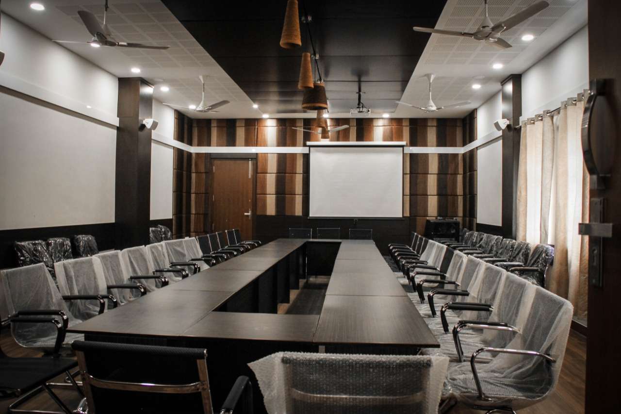 Contemporary boardroom interior with a central U-shaped conference table, acoustic ceiling panels, wood-accented walls, ceiling-mounted projector with screen – designed for corporate meetings and high-level discussions at corporate offices. - Designed by acoustic consultants, specialists at Coimbatore, India.