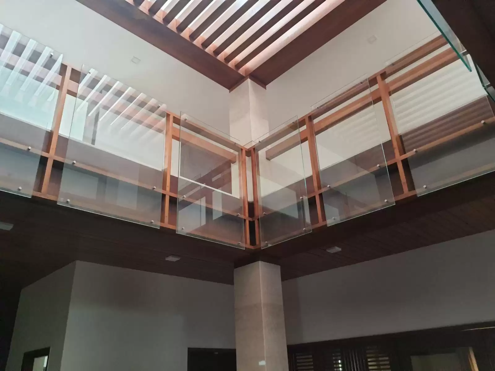 Modern wooden and glass balcony railing in a double-height living area with skylight ceiling design—custom interior execution by contractors in Perundurai, Erode, Tamilnadu.