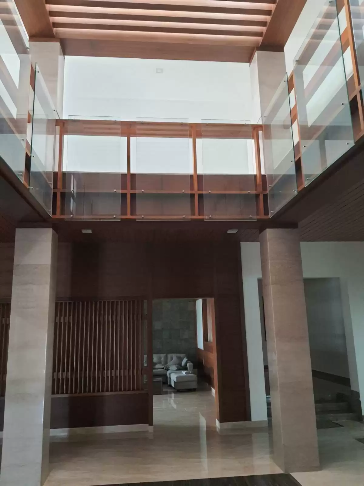 legant interior with wooden ceiling rafters, double-height glass and wood balcony railing, and stone wall living area—Designed, manufactured, and installed by our expert interior and furniture team in Coimbatore, Tamilnadu.