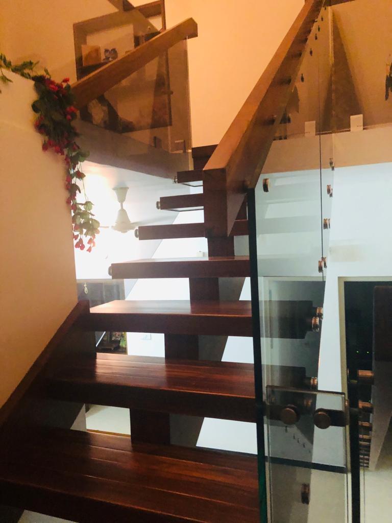 Steel-structured staircase with wooden cladding and sleek glass handrails, installed in a contemporary residence in Coimbatore — combining durability with elegant interior design.