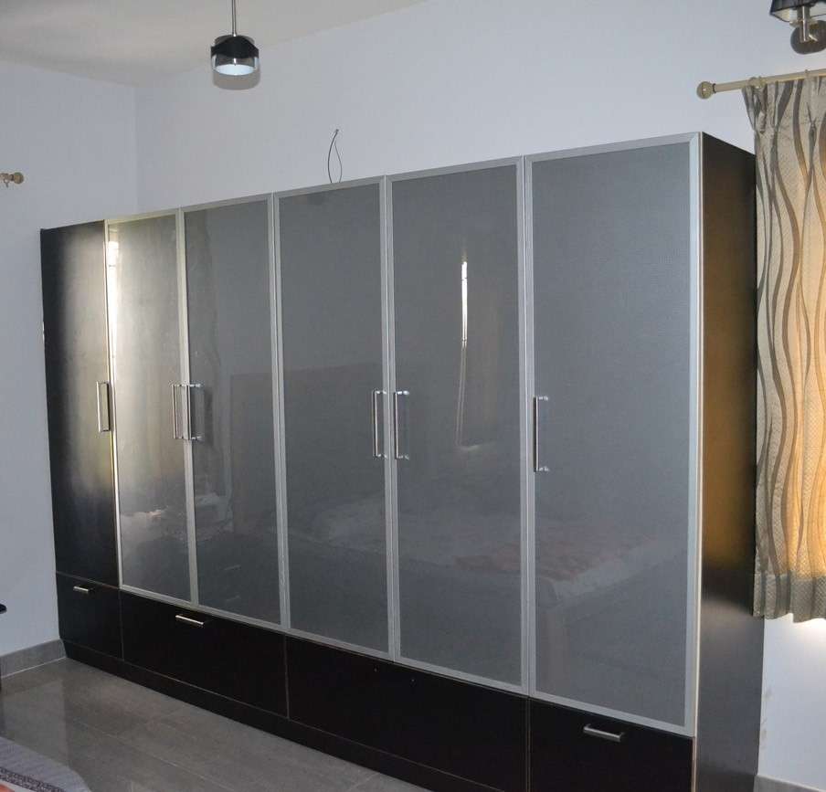 Sleek black modular wardrobe with lacquered glass shutters and brushed aluminum handles, featuring full-length storage and bottom drawers — bedroom interiors by professional interior designers in Erode, Tamilnadu.