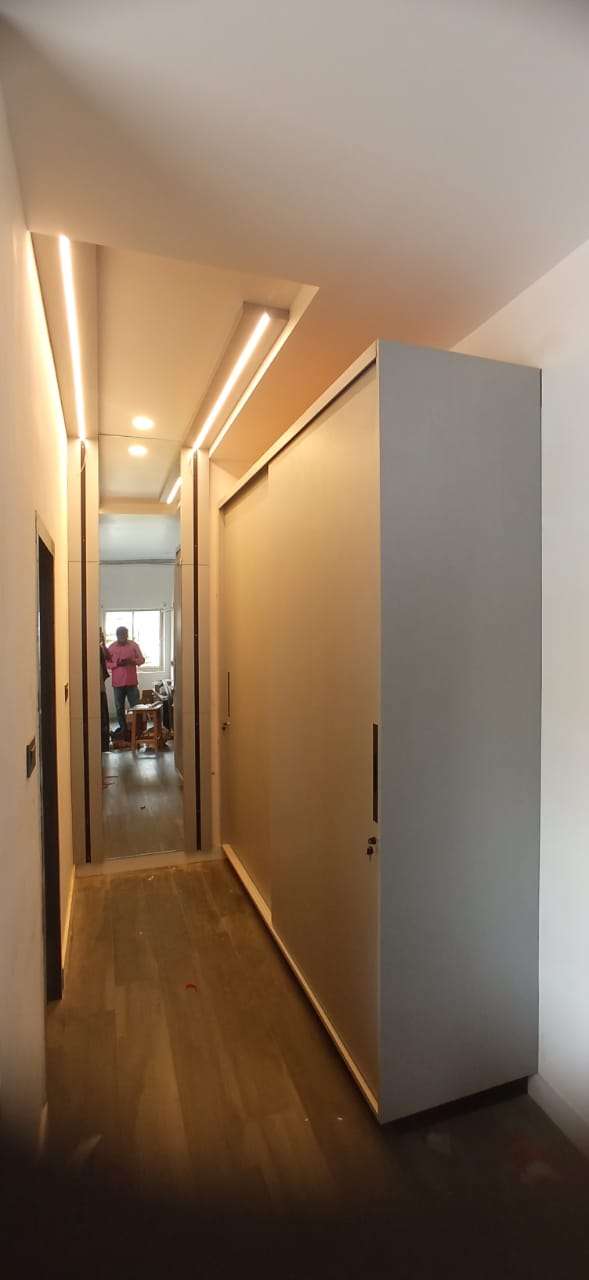 Full-height sliding wardrobe with minimalist handles and concealed storage, installed along a corridor with cove lighting and mirrored panels – Designed, manufactured, and installed by our expert interior and furniture team at Avinashi Road, Peelamedu, Coimbatore by expert modular wardrobe and furniture contractors.