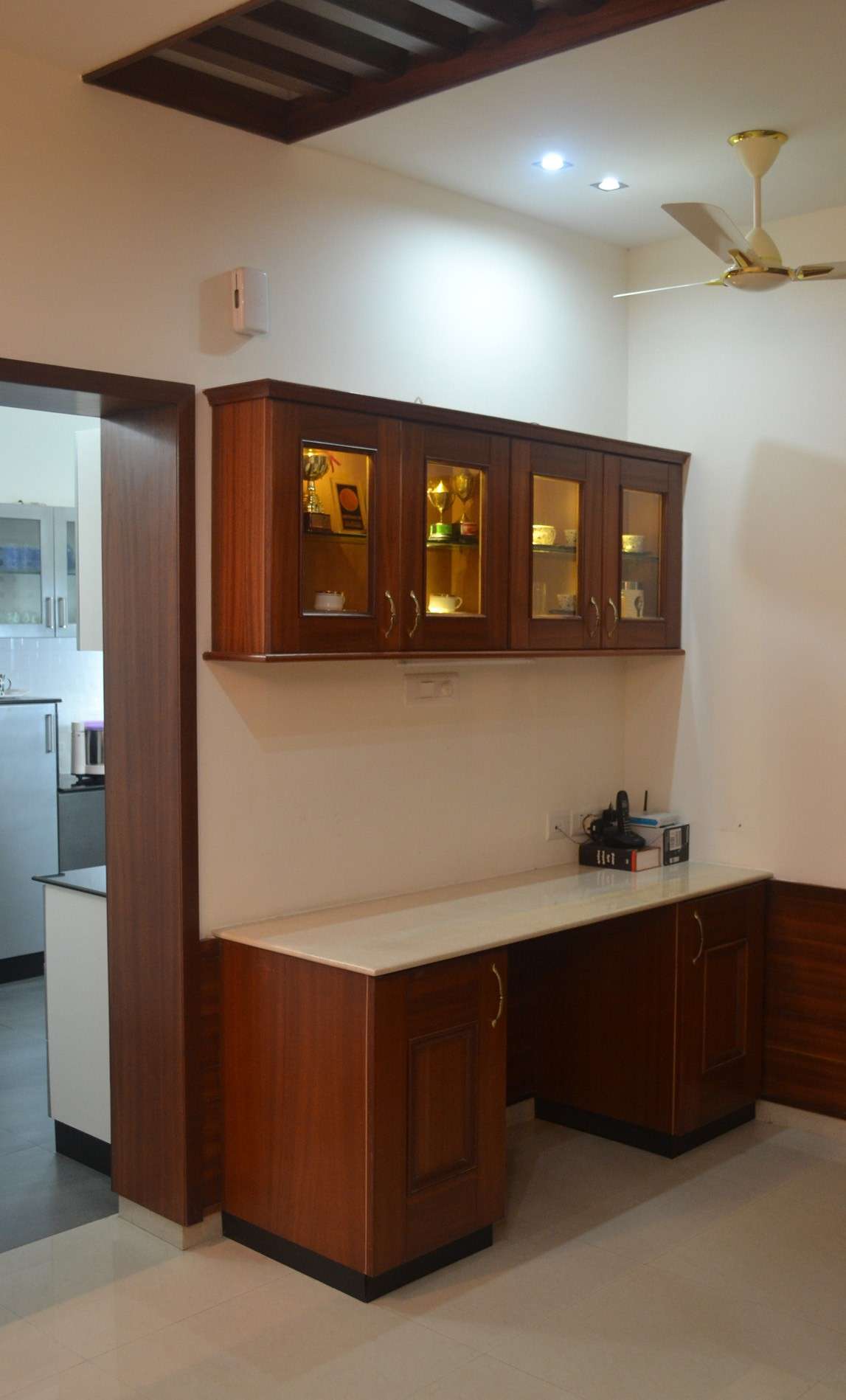 Wooden crockery and storage unit with glass-fronted overhead cabinets and marble countertop, custom-installed at a residence on Perundurai Road, Erode – designed by expert interior designers and contractors.