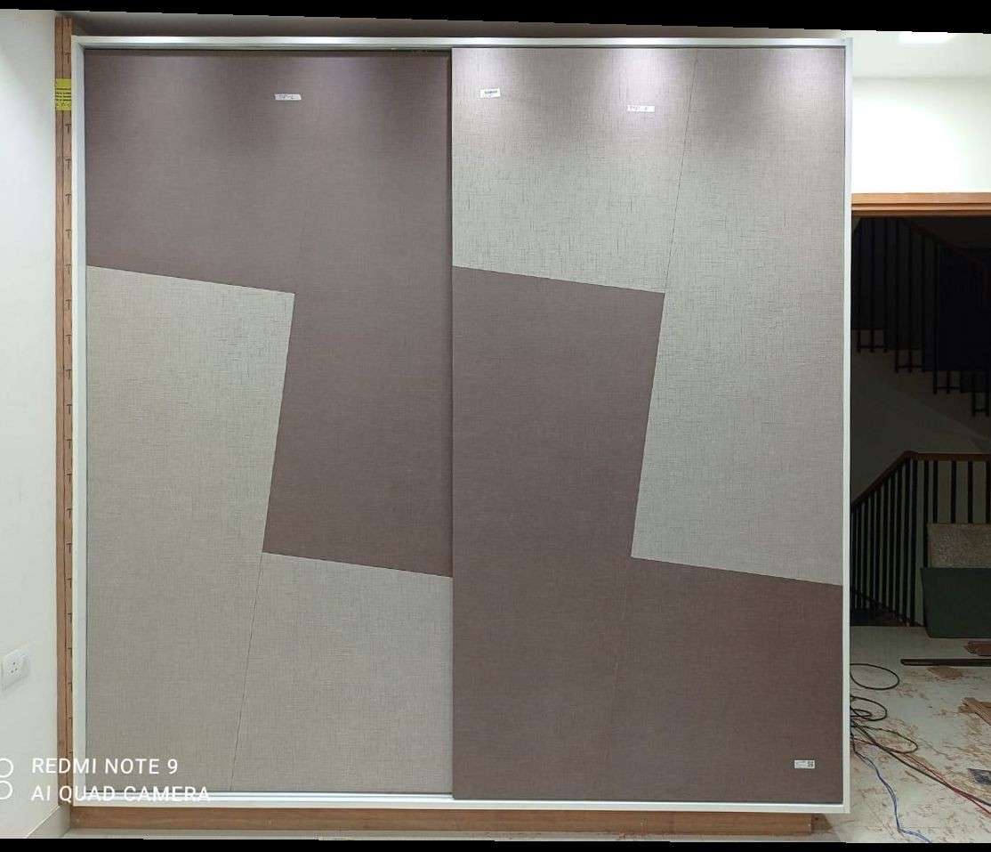 Designer sliding wardrobe with geometric dual-tone fabric-textured panels in brown and grey shades, illuminated by overhead spotlights – a premium modular wardrobe installation in Chennai, Tamil Nadu.