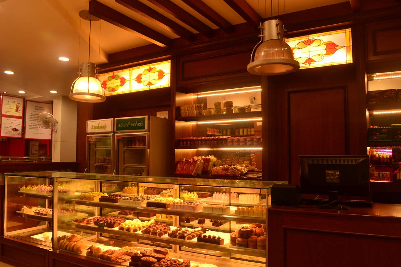 Richly designed bakery interior in Tamilnadu featuring classic wooden shelving, stained glass detailing, illuminated display counters with a wide range of cakes and pastries—executed by our expert interior design and furniture installation team.