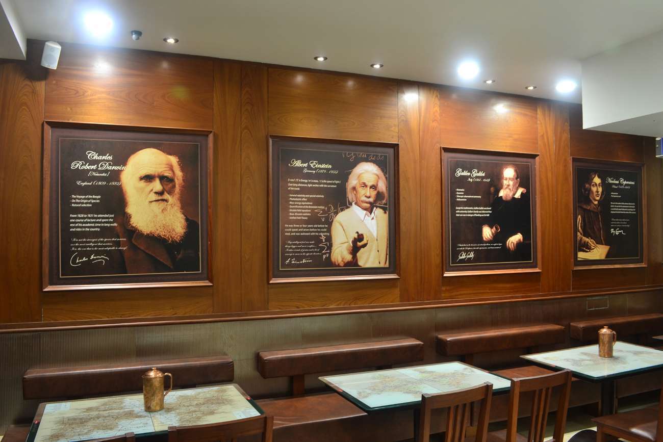 Wall-mounted portraits of famous scientists including Charles Darwin, Albert Einstein, and Galileo, enhancing the warm wooden interiors of a themed dining space in Tamilnadu — designed and executed by expert interior designers and contractors.