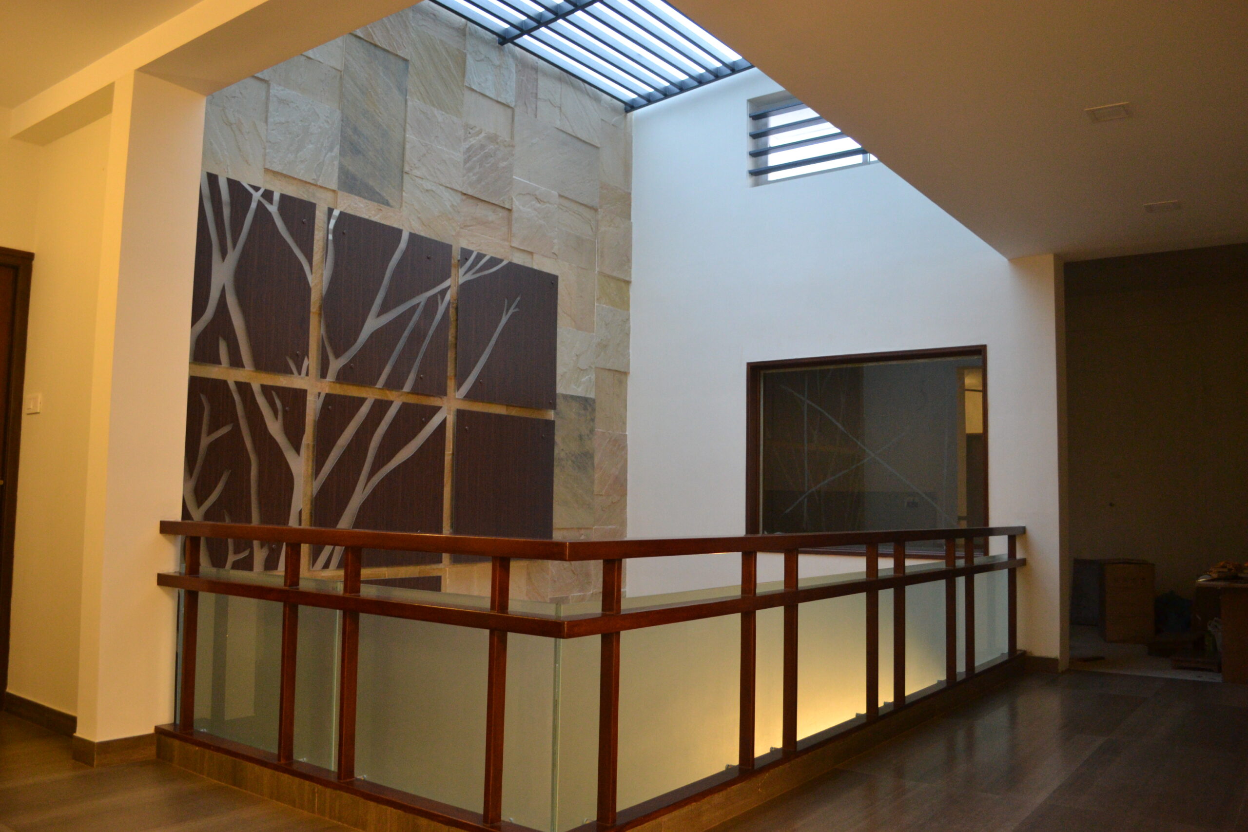 Elegant first-floor wooden railing with frosted glass panels and ambient lighting in a contemporary home interior in Tamil Nadu – custom designed and executed by interior specialists.