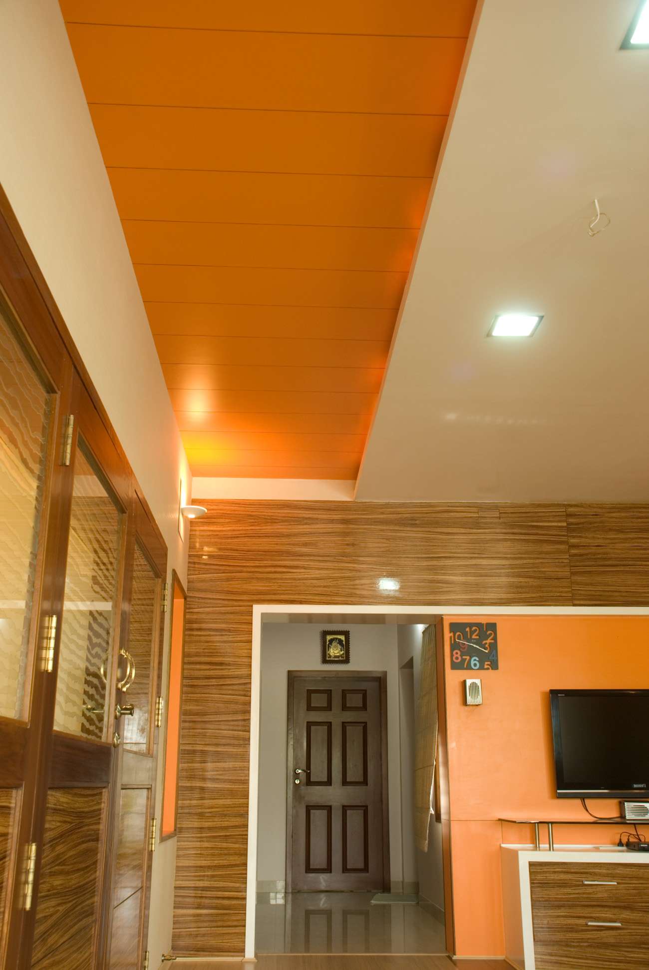 Vibrant orange false ceiling with matching wood-finish wall paneling and custom entertainment unit – designed and executed by our interior team in the rich living room of a residence project in Ooty near Coonoor, Tamil Nadu.