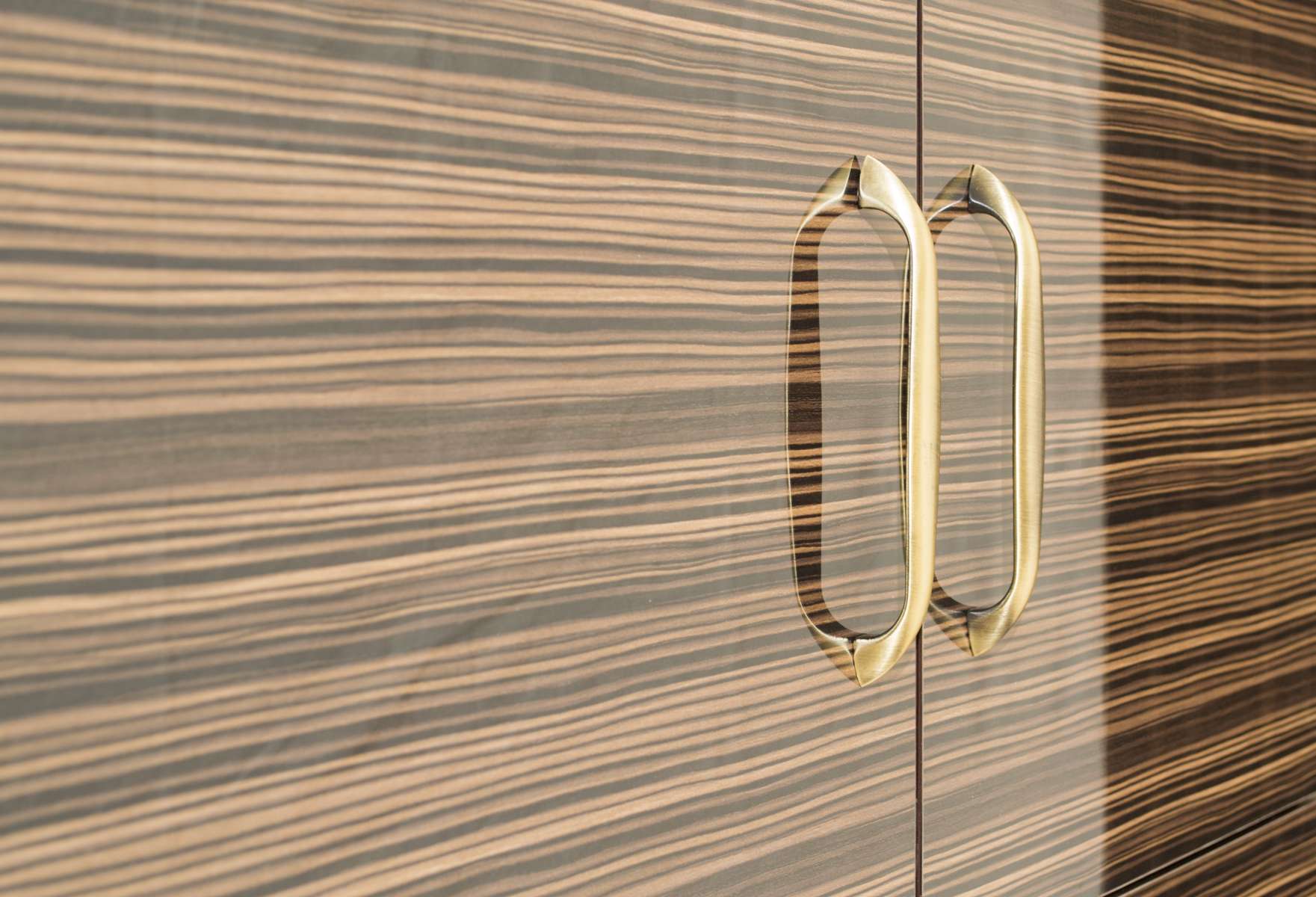 Brass-finish D-shaped handles on a high-gloss zebrawood laminate wardrobe — modern wardrobe design detail captured for luxury interior projects in Salem, Tamilnadu, India.