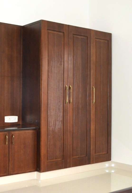 Teak wood - wooden wardrobe with classic panel shutters, brass handles, and integrated side cabinet — traditional solid wood wardrobe design executed by interior design experts in Annur, Tamilnadu, India.