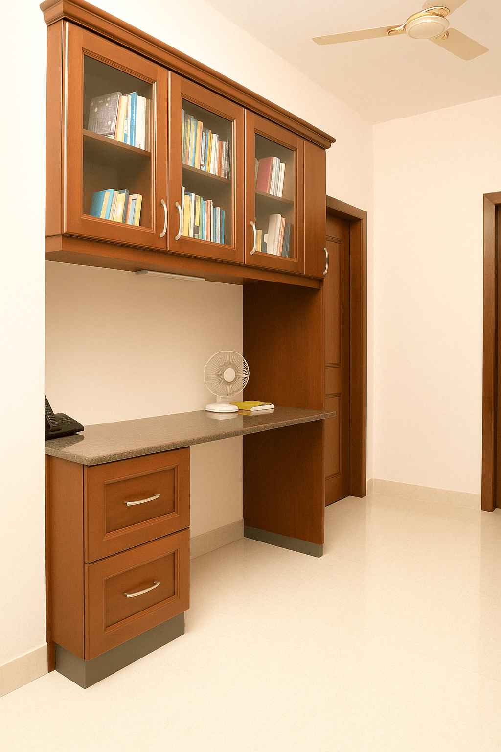 Wall-mounted wooden study and storage unit with overhead glass-front book cabinets and granite-finish worktop, designed for a residence in Palani, Tamil Nadu – crafted by professional interior designers and furniture contractors.