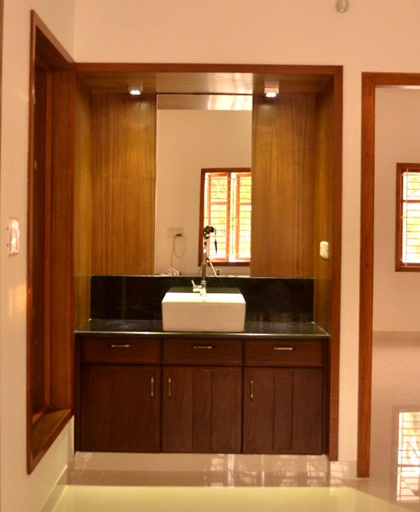 Contemporary hand wash counter with black granite top, under-sink wooden storage, and backlit vertical wood paneling with mirror – installed at a home in Sulur, Coimbatore by a professional interior designer and contractor.