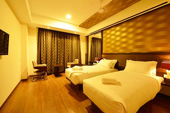 Elegant hotel room interior in Tamilnadu featuring twin beds, modern false ceiling with ambient lighting, wood-finish flooring, designer curtains, and custom furniture — done by hotel interior designers, turnkey contractors, furniture manufacturers, and hospitality space planners