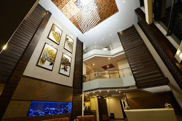 Grand hotel atrium interior at Erode, Tamilnadu featuring double-height ceiling, designer chandelier, modern artwork, glass railings, and a custom-built reception area — executed by expert hotel interior designers, contractors, and furniture manufacturers.
