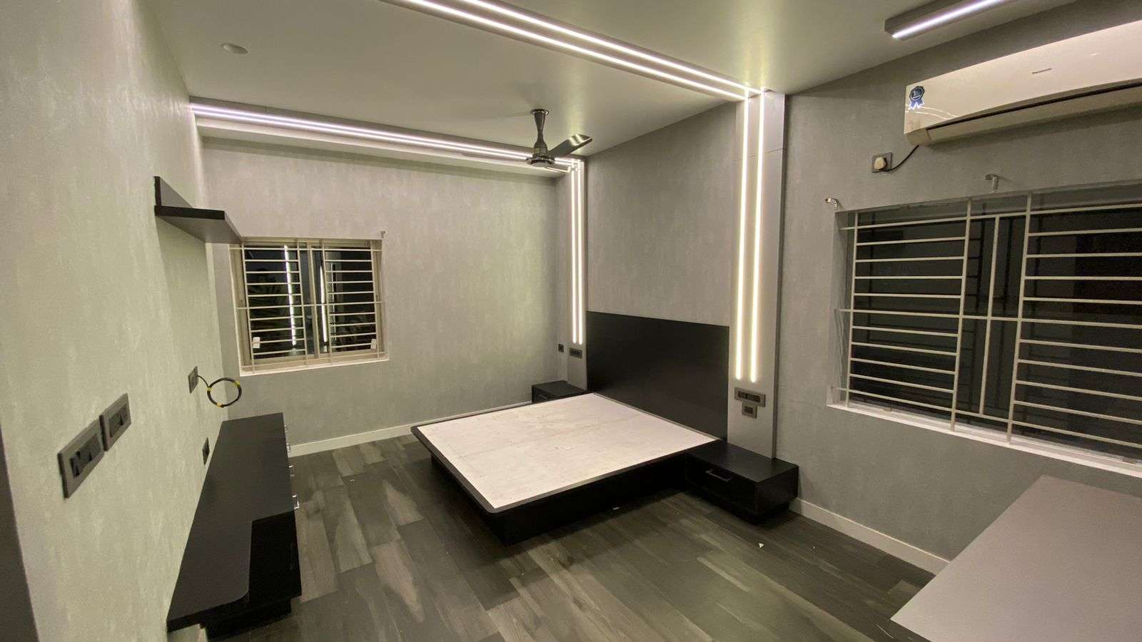 Modern black and grey themed bedroom with LED strip lighting, platform bed, and sleek custom woodwork designed for a college student in Avinashi Road, Peelamedu, Coimbatore.