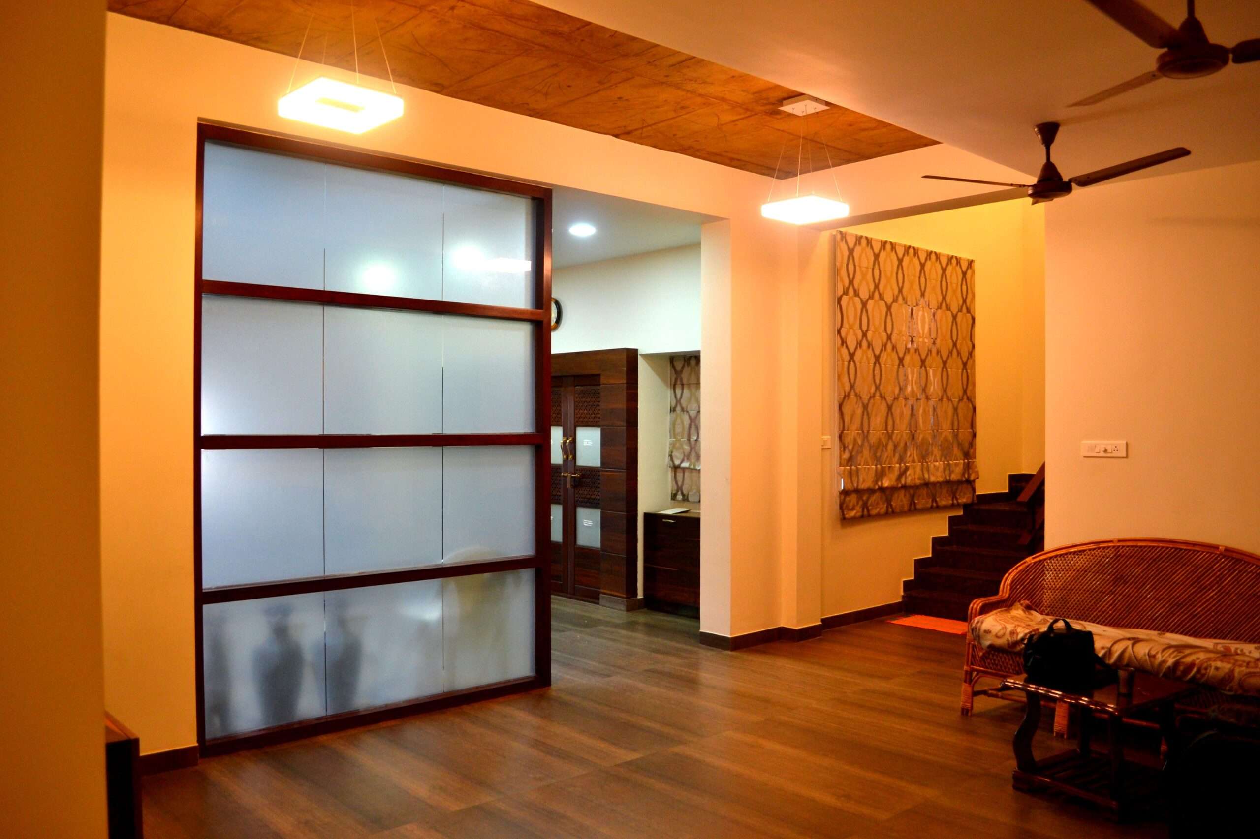 Warm living room interior with wooden flooring and a frosted glass partition framed in wood, designed, manufactured, and installed by our expert interior and furniture team in a residence at Chennai, Tamil Nadu.