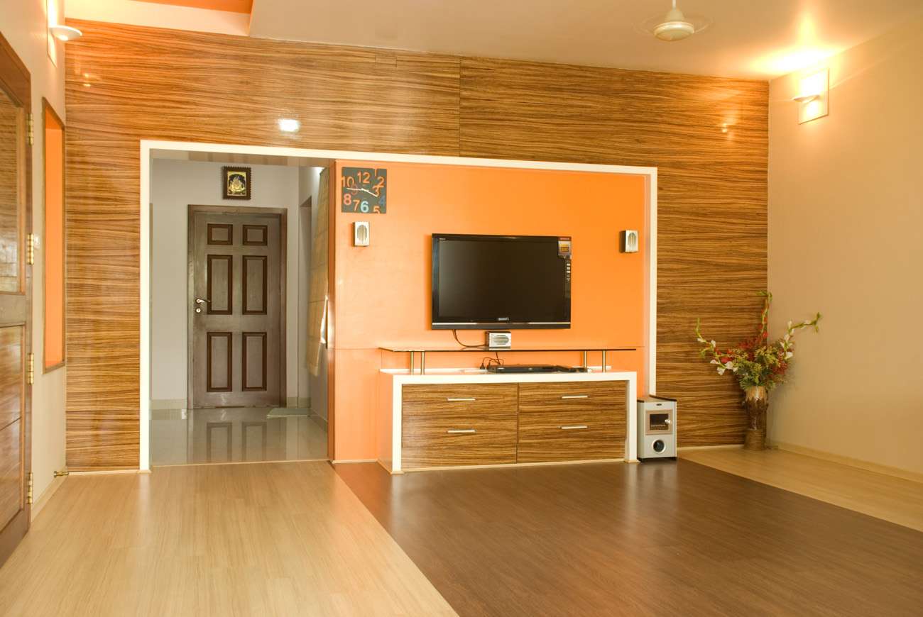 Contemporary living room interior featuring a modern TV unit with wood grain finish and orange accent wall, located at a residence in Salem, Tamil Nadu. Fully designed, manufactured, and installed by our expert interior and furniture team.