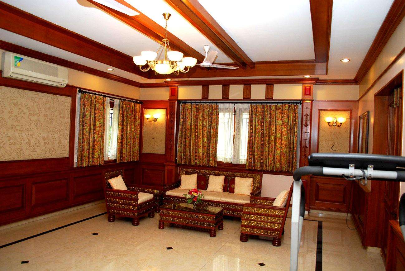Traditional European-style living room with carved wood furniture, decorative ceiling beams, and floral drapery at a residence in Udumalai, Udumalpet near Pollachi, Tamil Nadu. Fully designed, manufactured, and installed by our expert interior and furniture team.