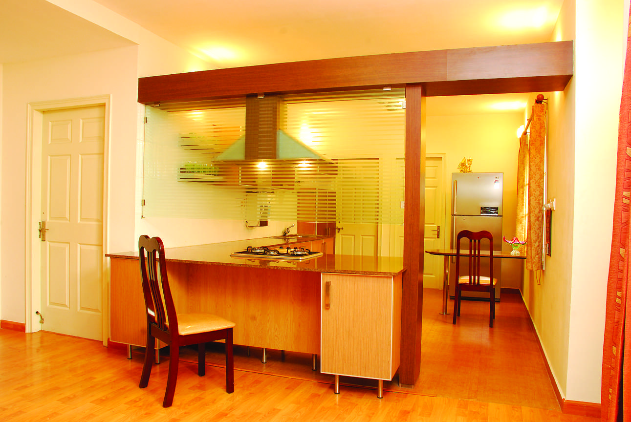 See-through modular kitchen in Avinashi, Tamil Nadu with glass partition, breakfast counter, and integrated hob visible from dining area. Fully designed, manufactured, and installed by our expert interior and furniture team.