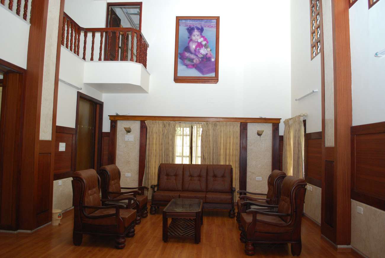 Double-height living room interior with classic wooden furniture, upper-level balcony, and natural light at a residence in Coonoor near Ooty, Tamil Nadu. Fully designed, manufactured, and installed by our expert interior and furniture team.