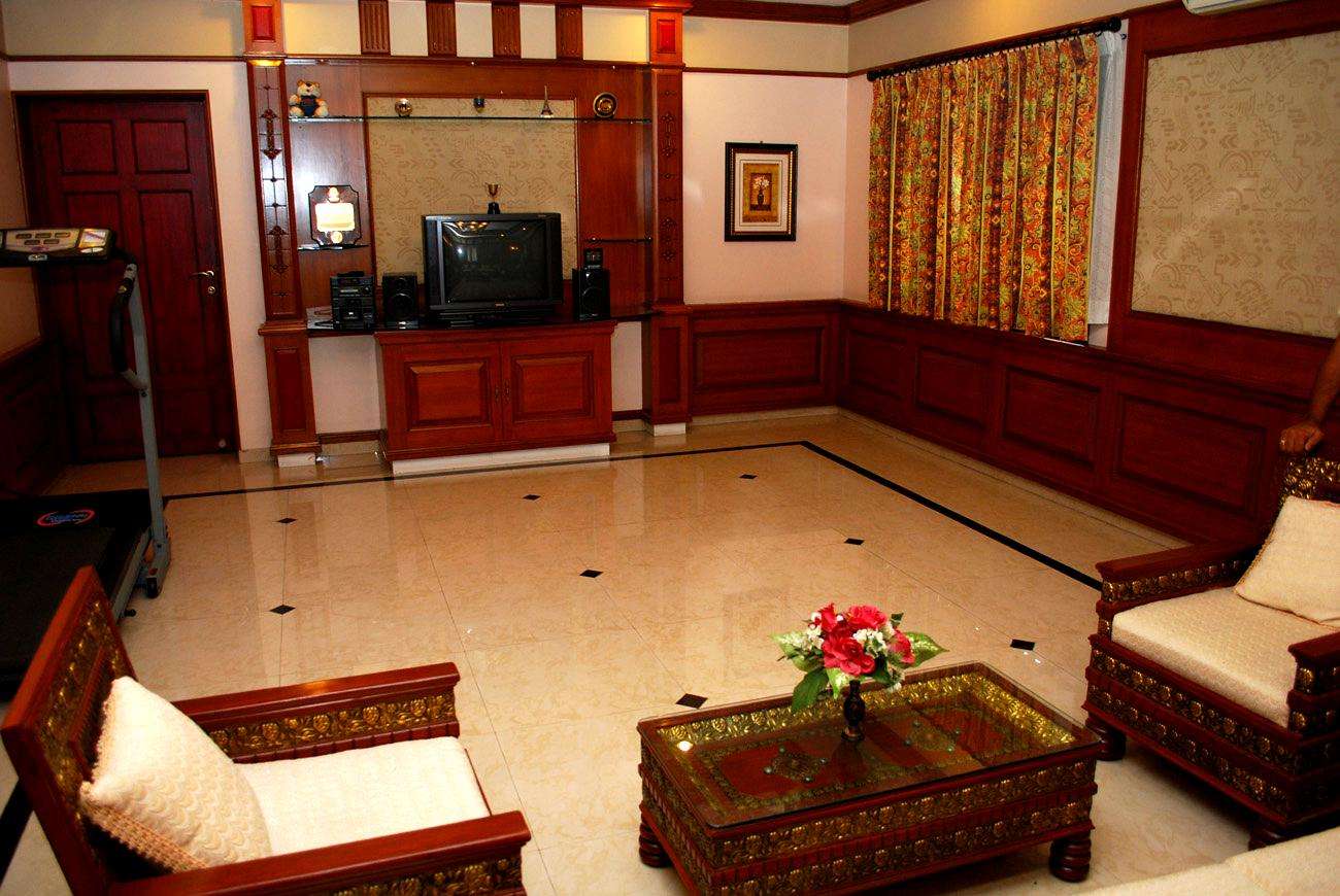 Traditional living room interior with walnut-colored woodwork, classic furniture, and floral curtains in an apartment at Avinashi Road, Coimbatore. Fully designed, manufactured, and installed by our expert interior and furniture team.