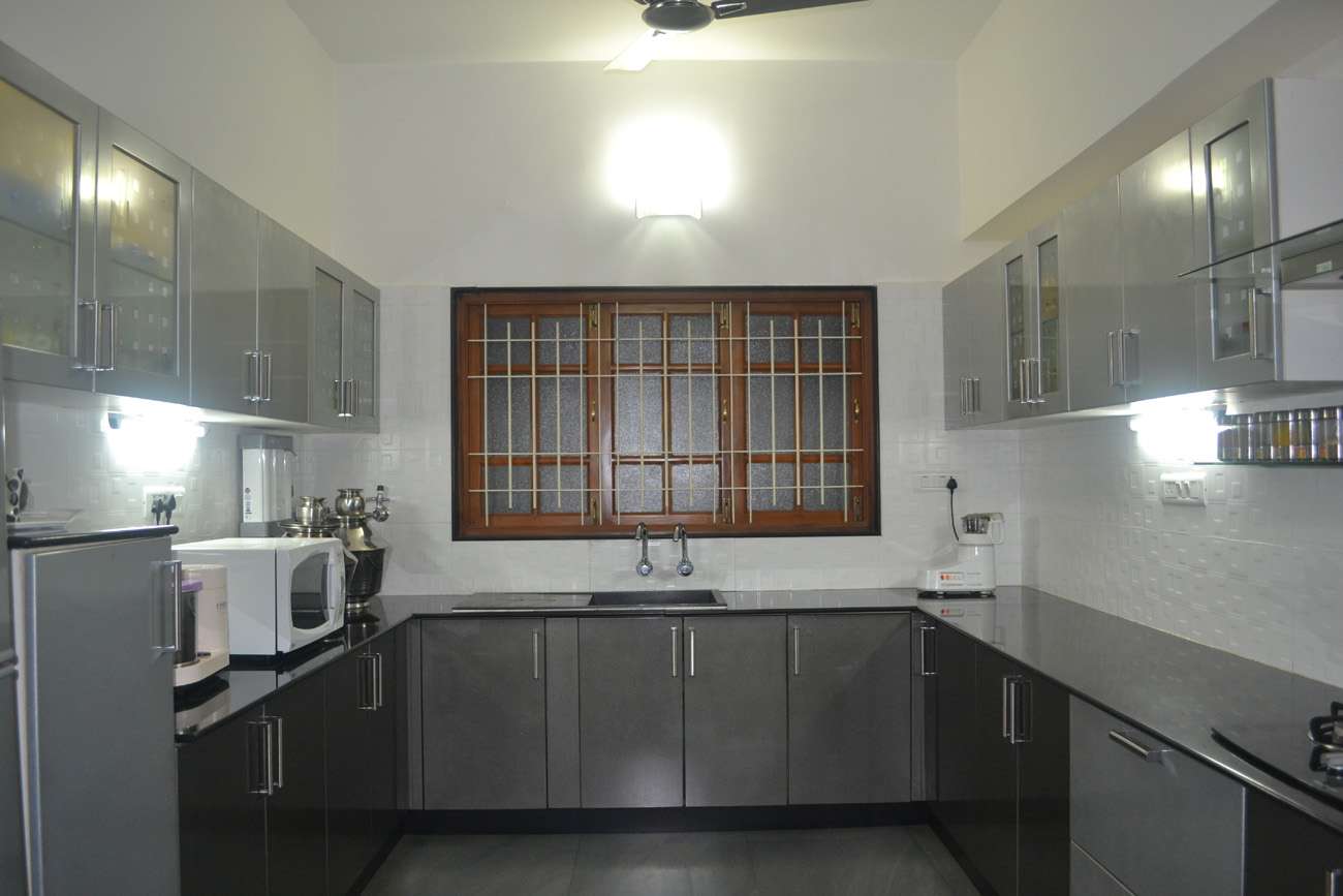 Modular kitchen in Tiruppur featuring black and grey lacquered glass shutters, sleek handles with U-shaped layout. Fully designed, manufactured, and installed by our expert interior and furniture team.